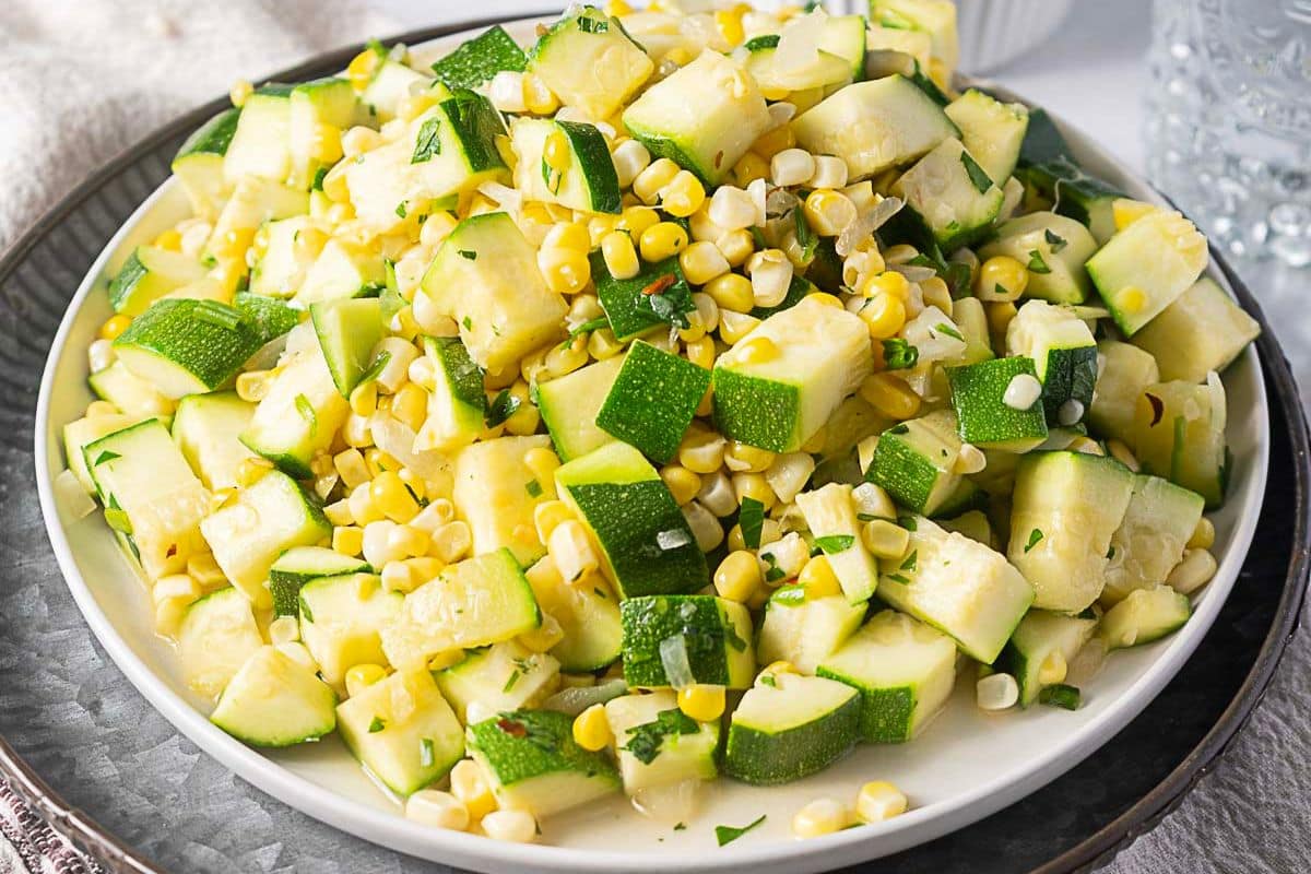 A plate of diced zucchini and corn mixed with herbs, served on a white dish—perfect for creative zucchini recipes and delicious summer recipes.