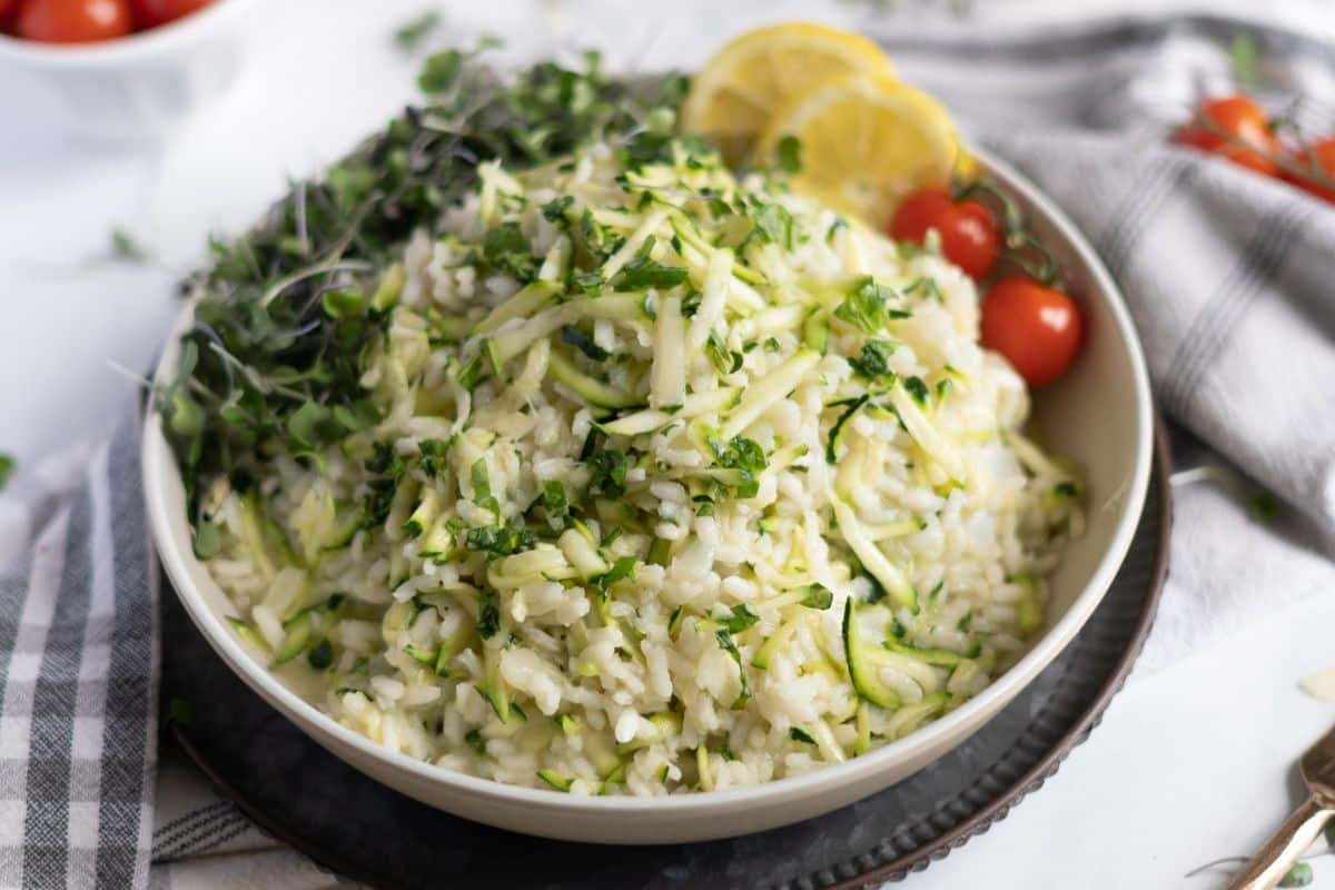 A bowl of rice mixed with shredded zucchini, topped with microgreens, served with cherry tomatoes and lemon slices on the side—a fresh twist for creative zucchini recipes.