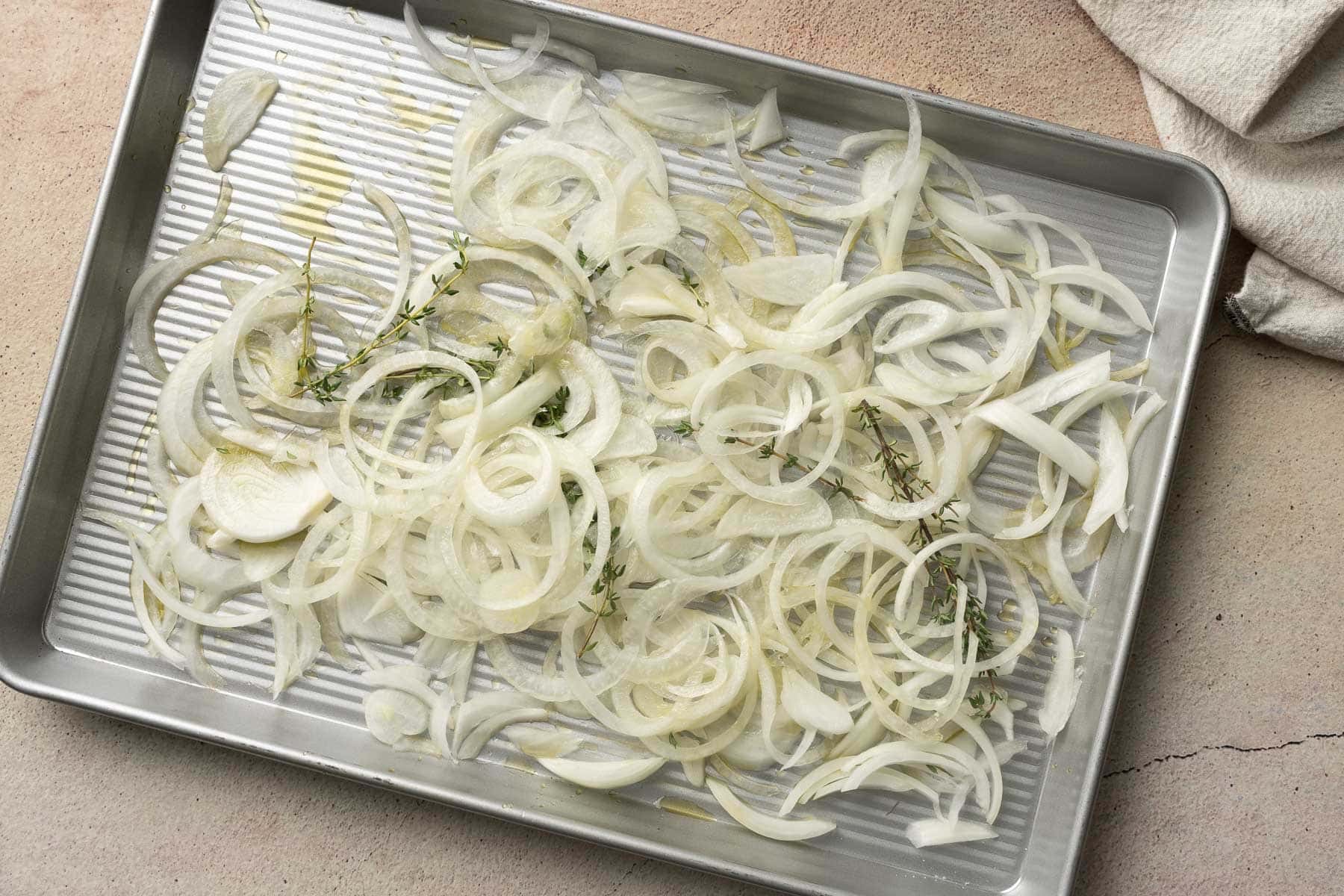 A baking sheet with Baked Lamb Shoulder Chops nestled among thinly sliced onions and sprigs of thyme, soon to become caramelized onions.