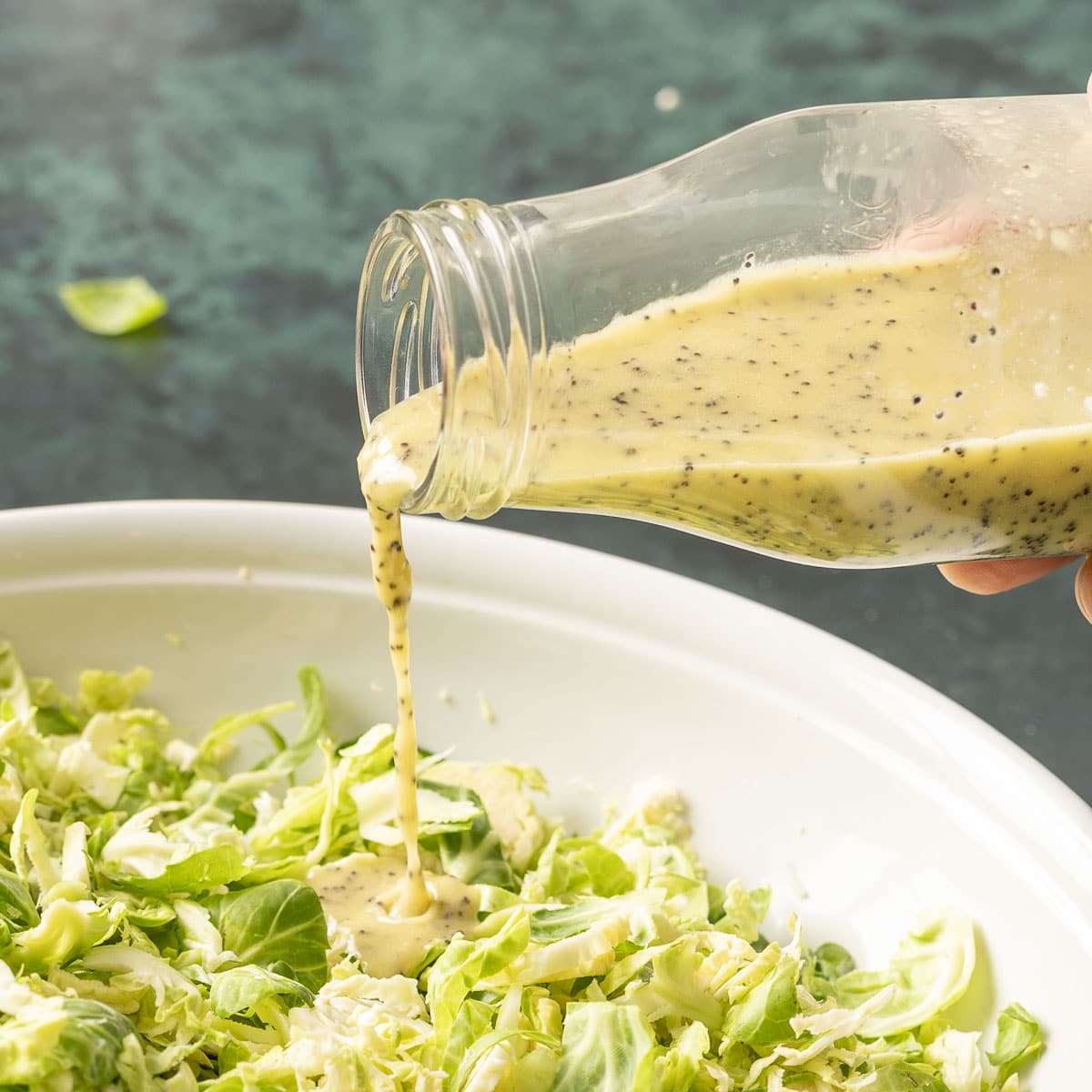 pouring poppyseed dressing on a salad.