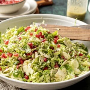shaved brussels sprout salad with pomegranate in a white serving bowl.