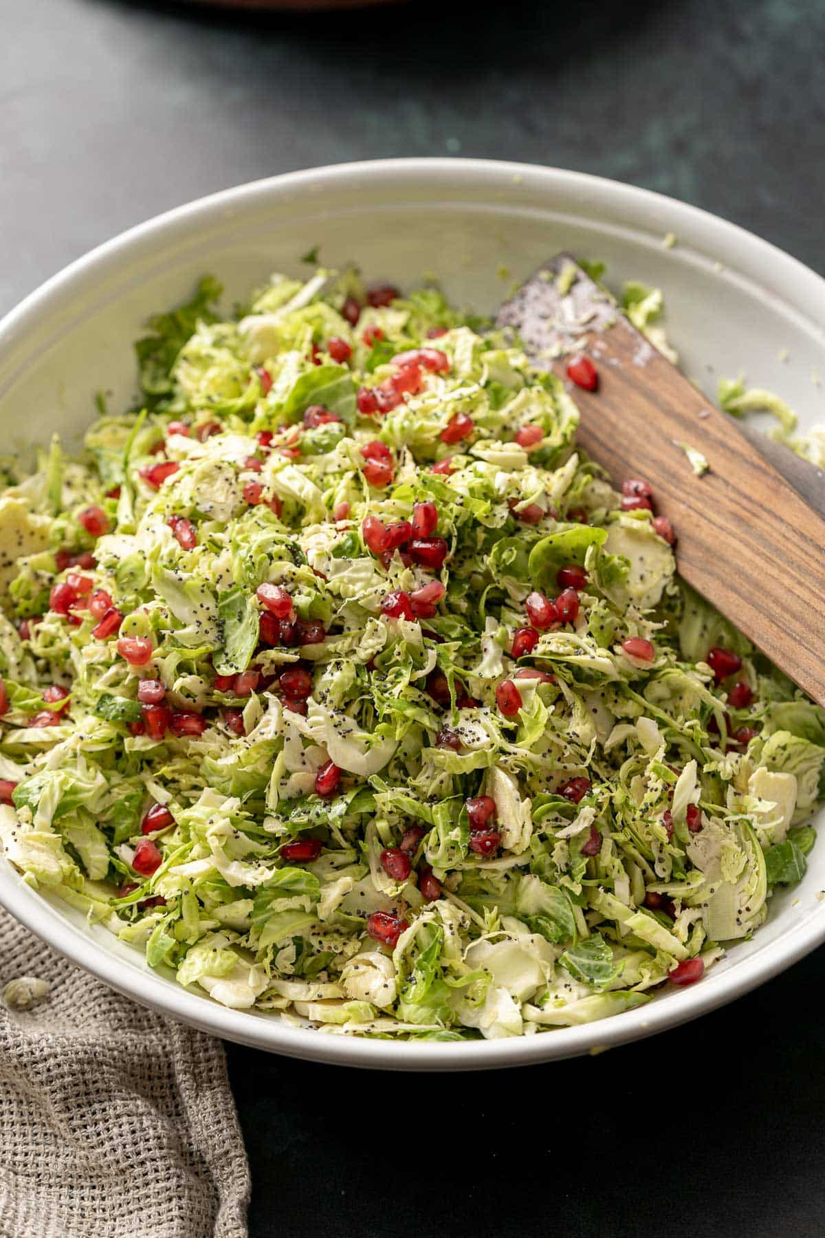 shaved brussels sprout salad with pomegranate in a white serving bowl with wood utensils.