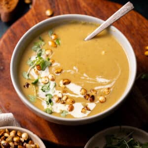 Delicata squash soup in a bowl with cream, microgreens and a spoon.
