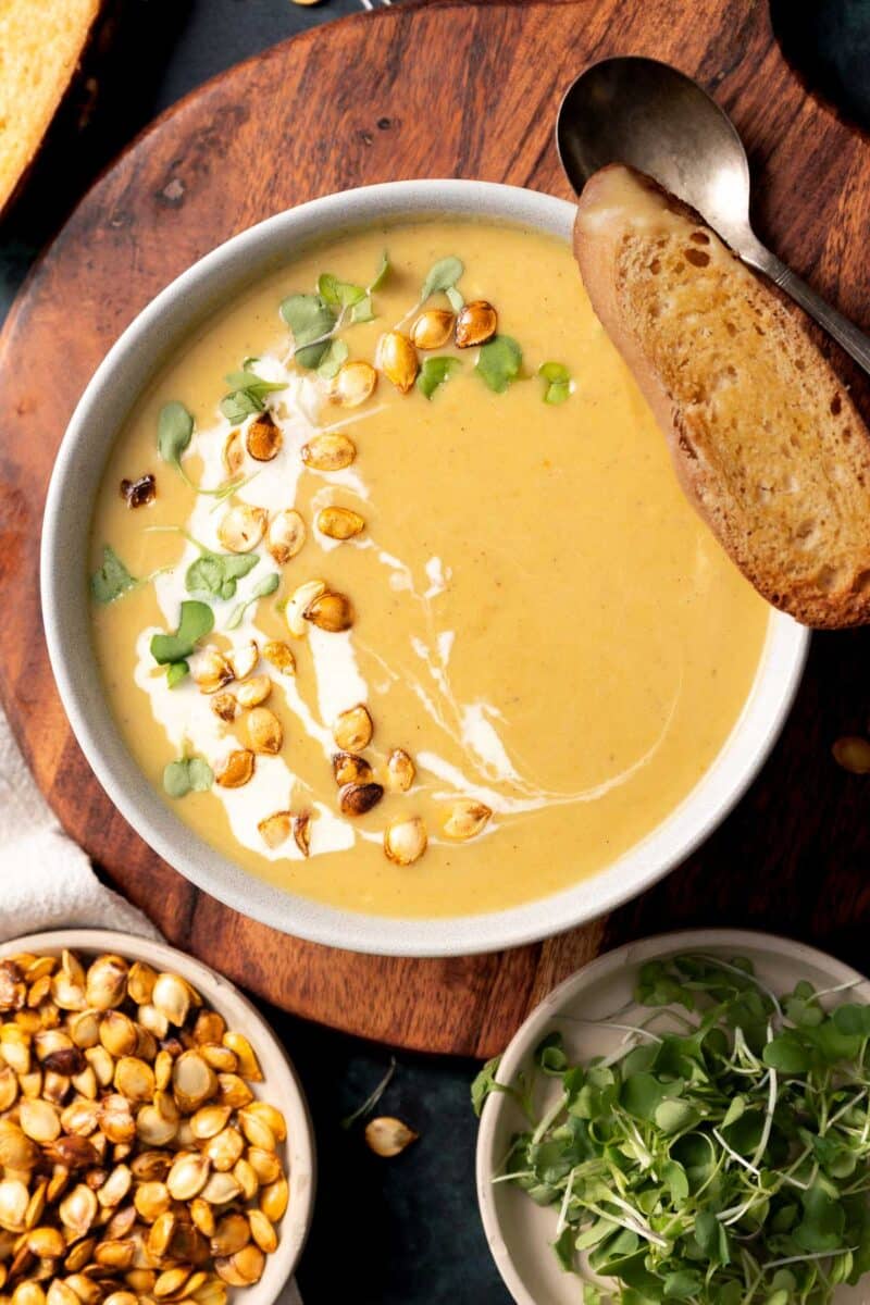 Delicata squash soup in a bowl with a swirl of cream, microgreens and a piece of toasted bread.