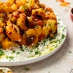 A plate of harissa cauliflower florets garnished with chopped herbs and served on a white sauce, with a sprinkle of herbs on top.