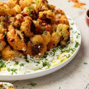 A plate of harissa cauliflower florets garnished with chopped herbs and served on a white sauce, with a sprinkle of herbs on top.