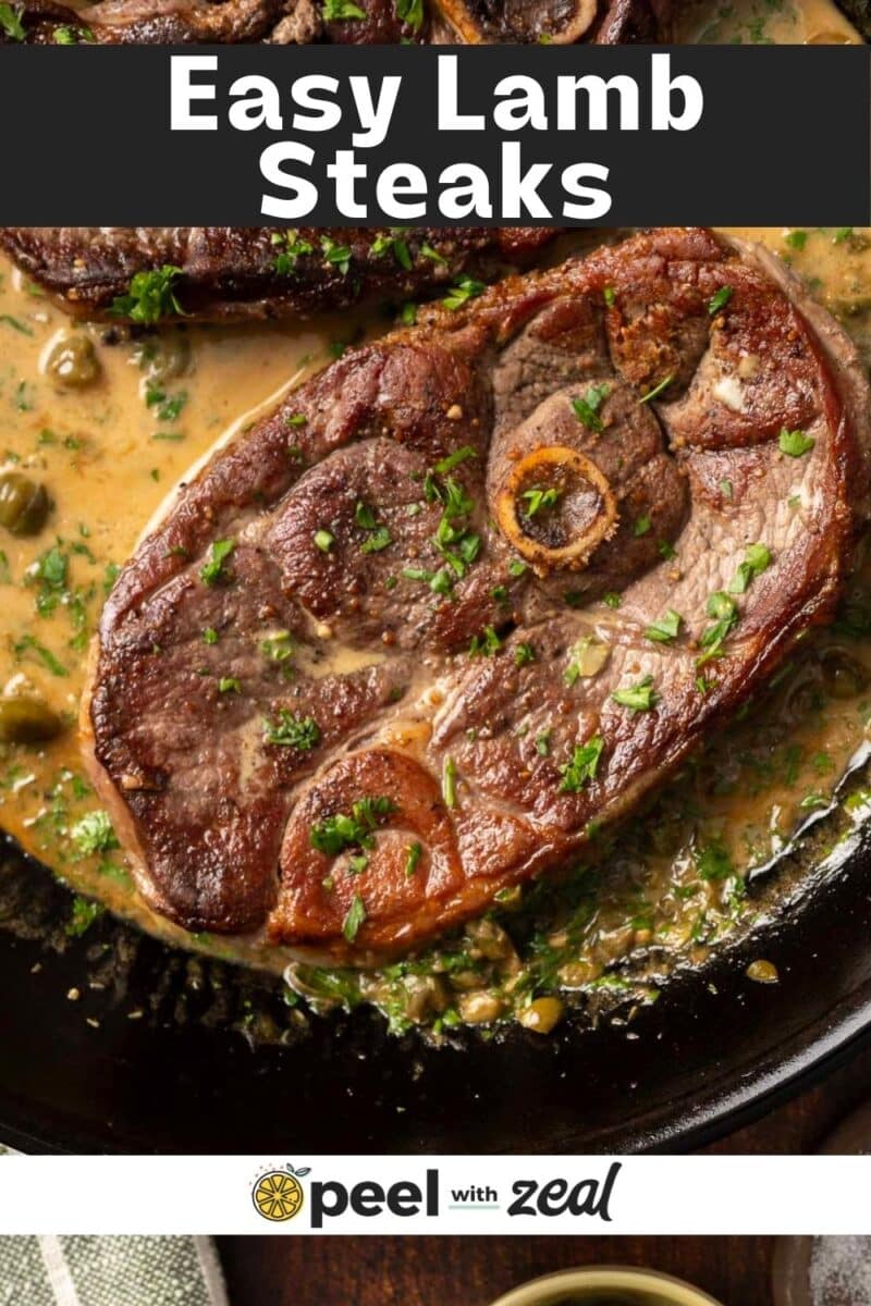 Close-up of cooked lamb steaks in a creamy sauce, garnished with parsley, displayed in a black skillet. "Easy Lamb Steaks" is written on a banner at the top, with "peel with zeal" at the bottom.