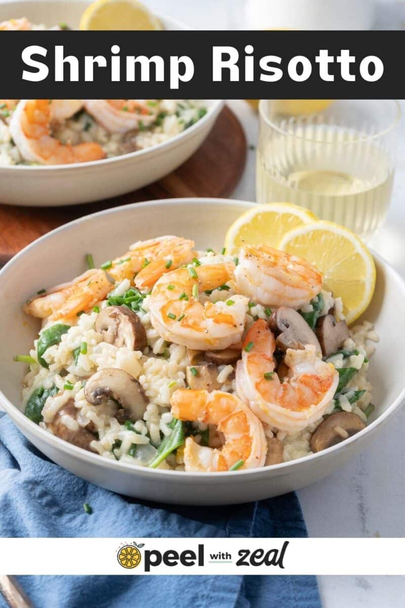 A bowl of shrimp risotto with mushrooms and greens, garnished with lemon slices. Another bowl and a glass of white wine in the background. The text "Shrimp Risotto" is at the top of the image.