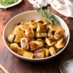 Roasted parsnips in a bowl with a sprig of rosemary.