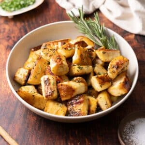 Roasted parsnips in a bowl with a sprig of rosemary.