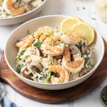 A bowl of shrimp risotto garnished with lemon slices and herbs on a wooden board.