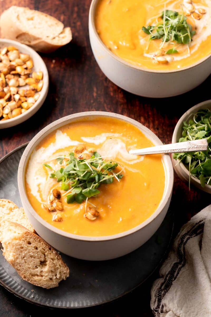 Carrot squash soup in a bowl with a swirl of cream, microgreens and a piece of toasted bread.