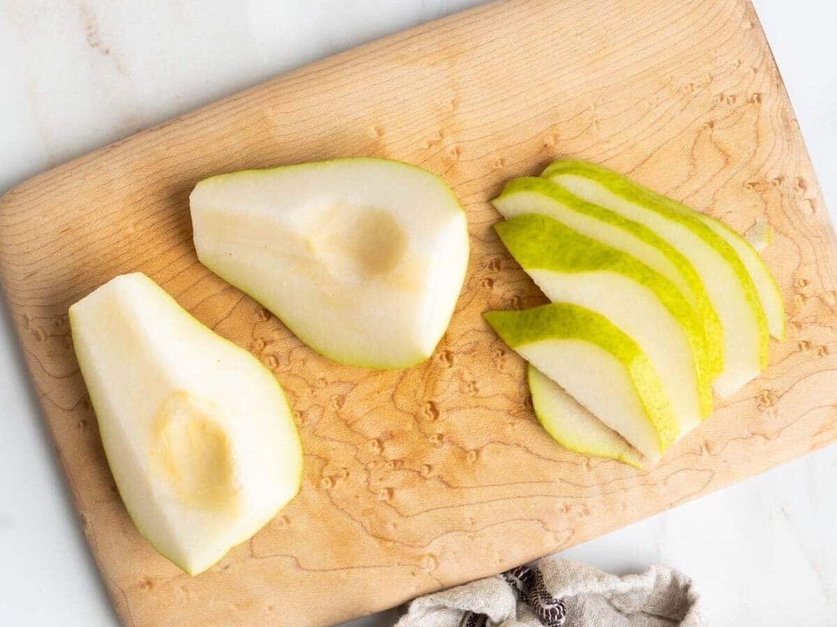Pear sliced vertically on a wooden chopping board.
