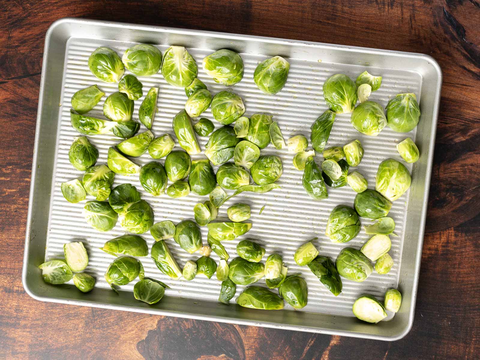 A baking sheet filled with raw Brussels sprouts, some cut in half, awaits transformation into a delicious roasted Brussels sprout salad on a rustic wooden surface.