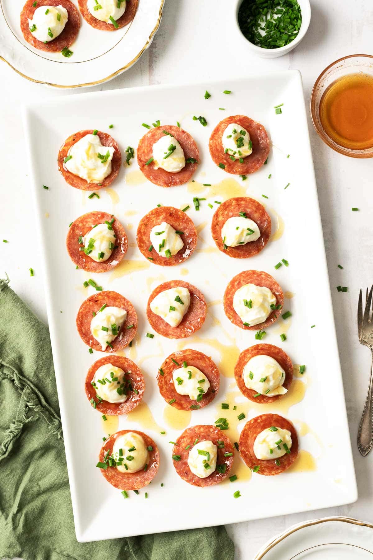 A platter of salami chips topped with honey whipped ricotta and garnished with chopped herbs.