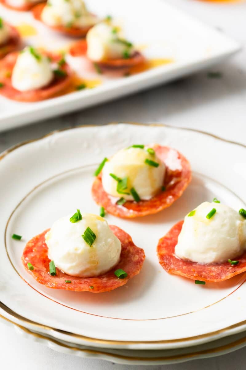Plated appetizers featuring pepperoni slices topped with mozzarella balls, garnished with chopped chives, and paired perfectly with a side of honey whipped ricotta.