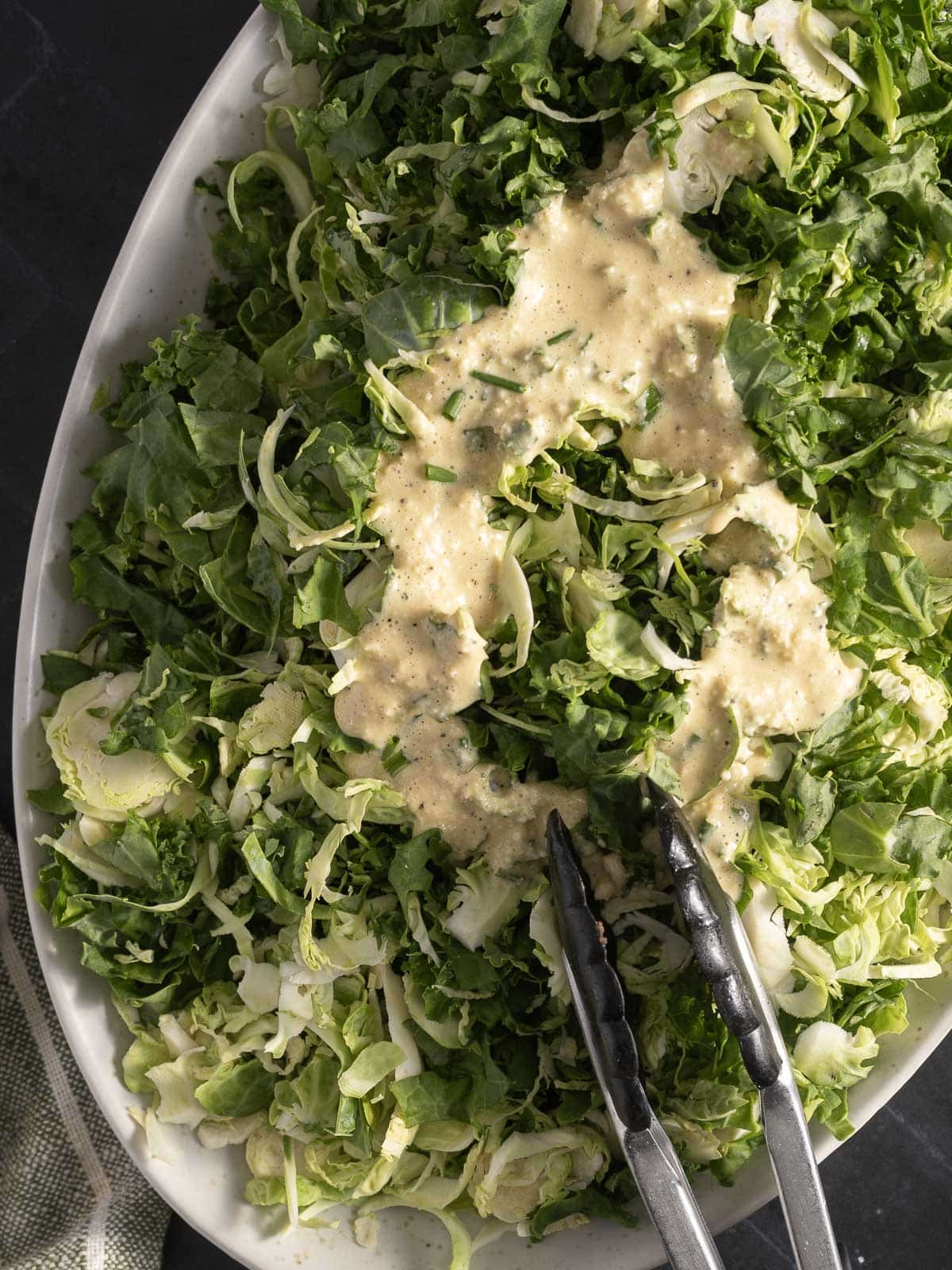 A platter of chopped greens topped with a creamy anchovy Caesar dressing, with metal tongs resting on the side.