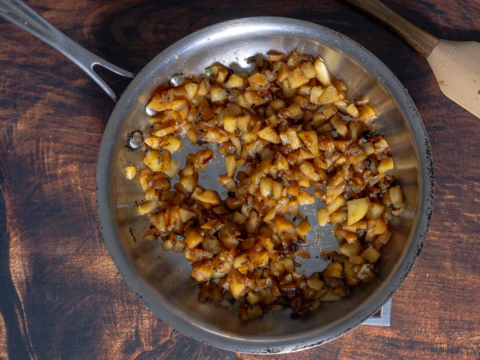 Diced onions sizzle in a stainless steel pan on a wooden surface, creating the perfect aromatic base for a delicious crostini topped with creamy brie and crisp apple slices.