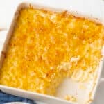 A baking dish with baked macaroni and cheese, partially served, showing creamy pasta beneath a golden, cheesy crust.