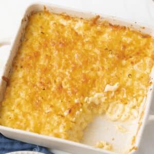 A baking dish with baked macaroni and cheese, partially served, showing creamy pasta beneath a golden, cheesy crust.