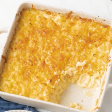 A baking dish with baked macaroni and cheese, partially served, showing creamy pasta beneath a golden, cheesy crust.