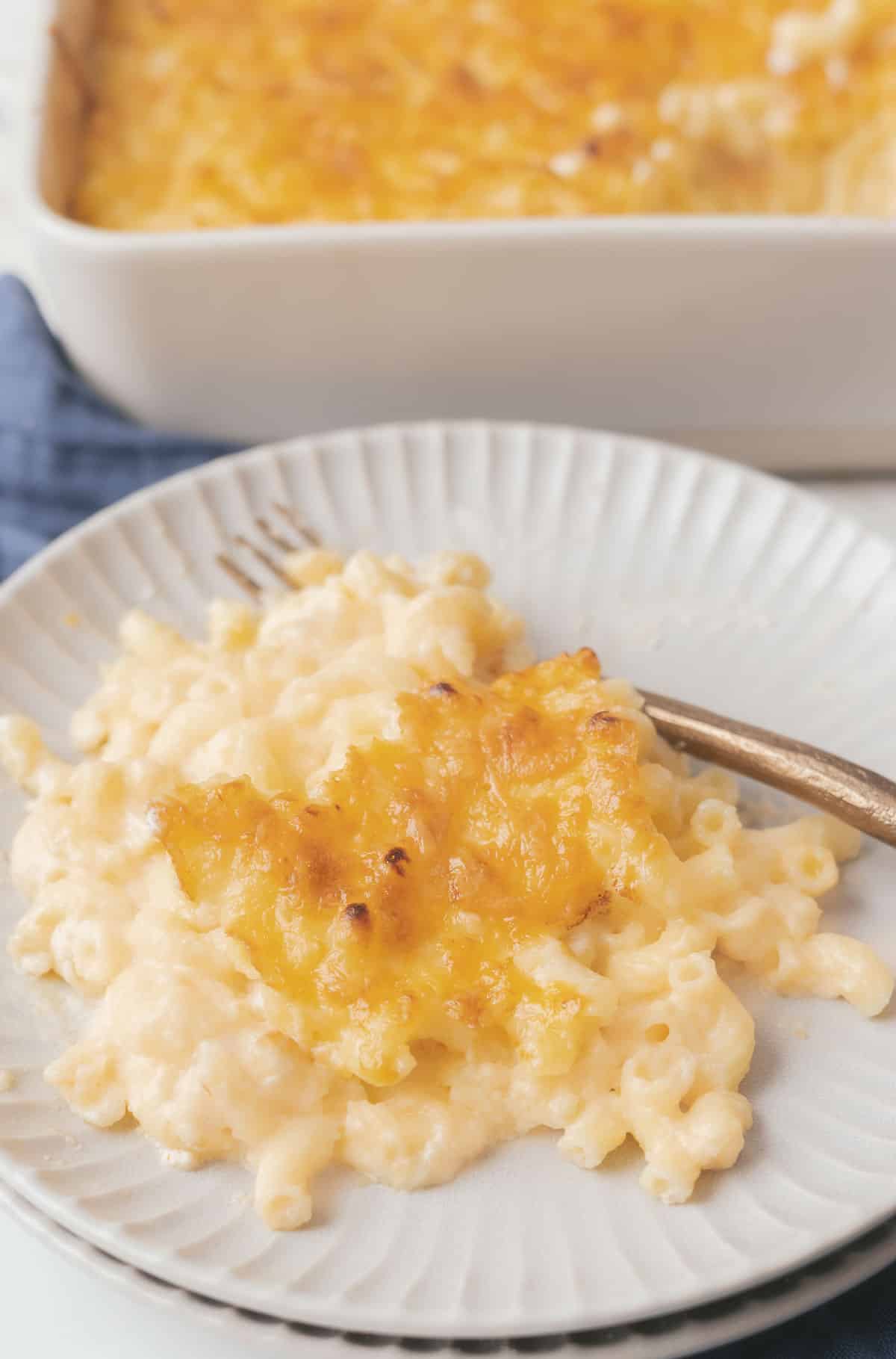 A serving of baked macaroni and cheese on a plate with a fork, featuring a golden brown cheese topping.