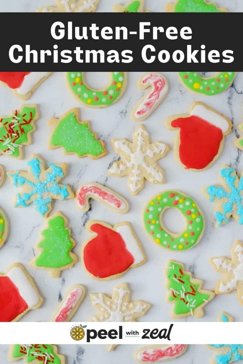 Colorful gluten-free Christmas cookies in various shapes like mittens, snowflakes, and wreaths on a white surface.