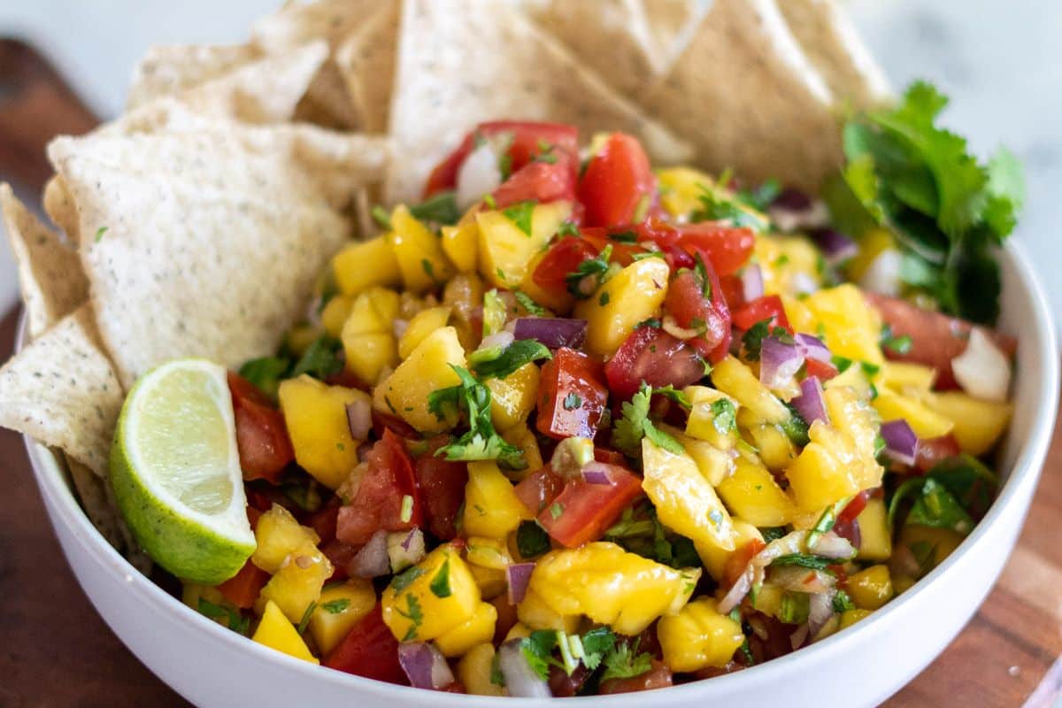 A bowl of mango salsa with diced mango, tomatoes, onions, cilantro, and lime, accompanied by tortilla chips.
