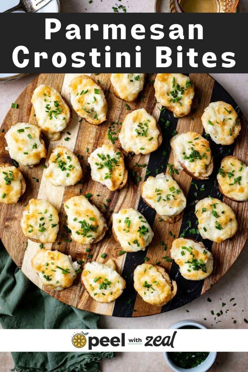 Wooden board with Parmesan crostini topped with herbs, arranged neatly. A green cloth and napkin are visible beneath.