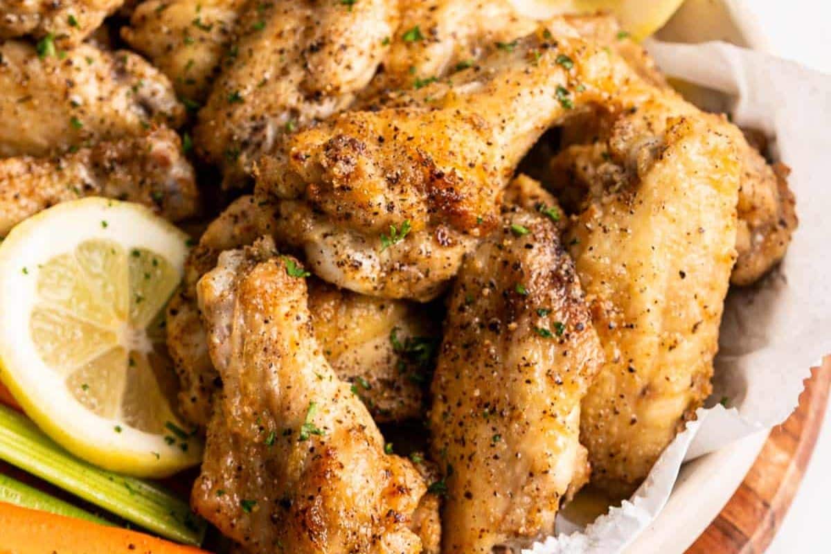 A plate of seasoned and baked chicken wings with lemon slices and celery sticks.