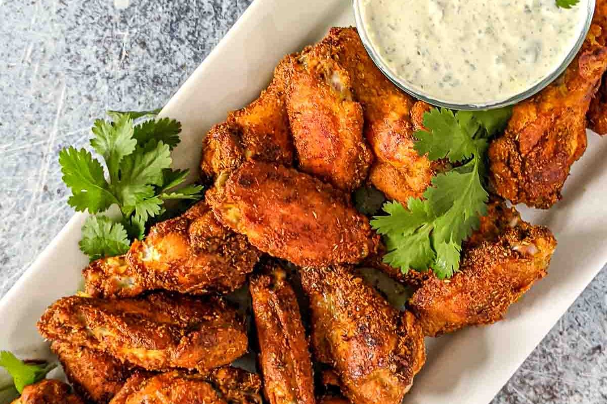 A plate of crispy seasoned chicken wings garnished with cilantro, served with a small bowl of creamy dip.