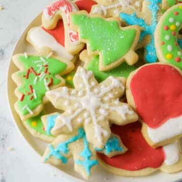 A plate of vibrant, gluten-free cut-out sugar cookies adorned with snowflakes, Christmas trees, and Santa hats, all topped with festive icing and sprinkles.