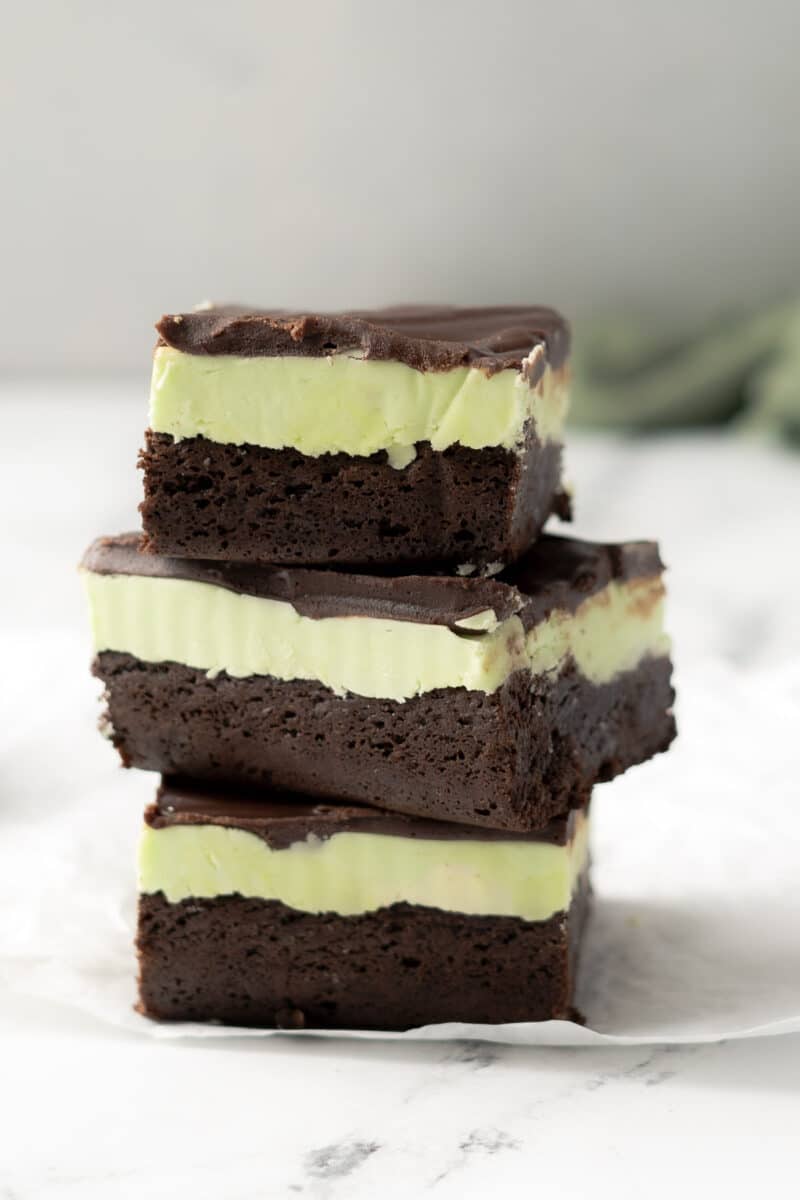Three gluten-free chocolate mint brownies stacked on a white surface.