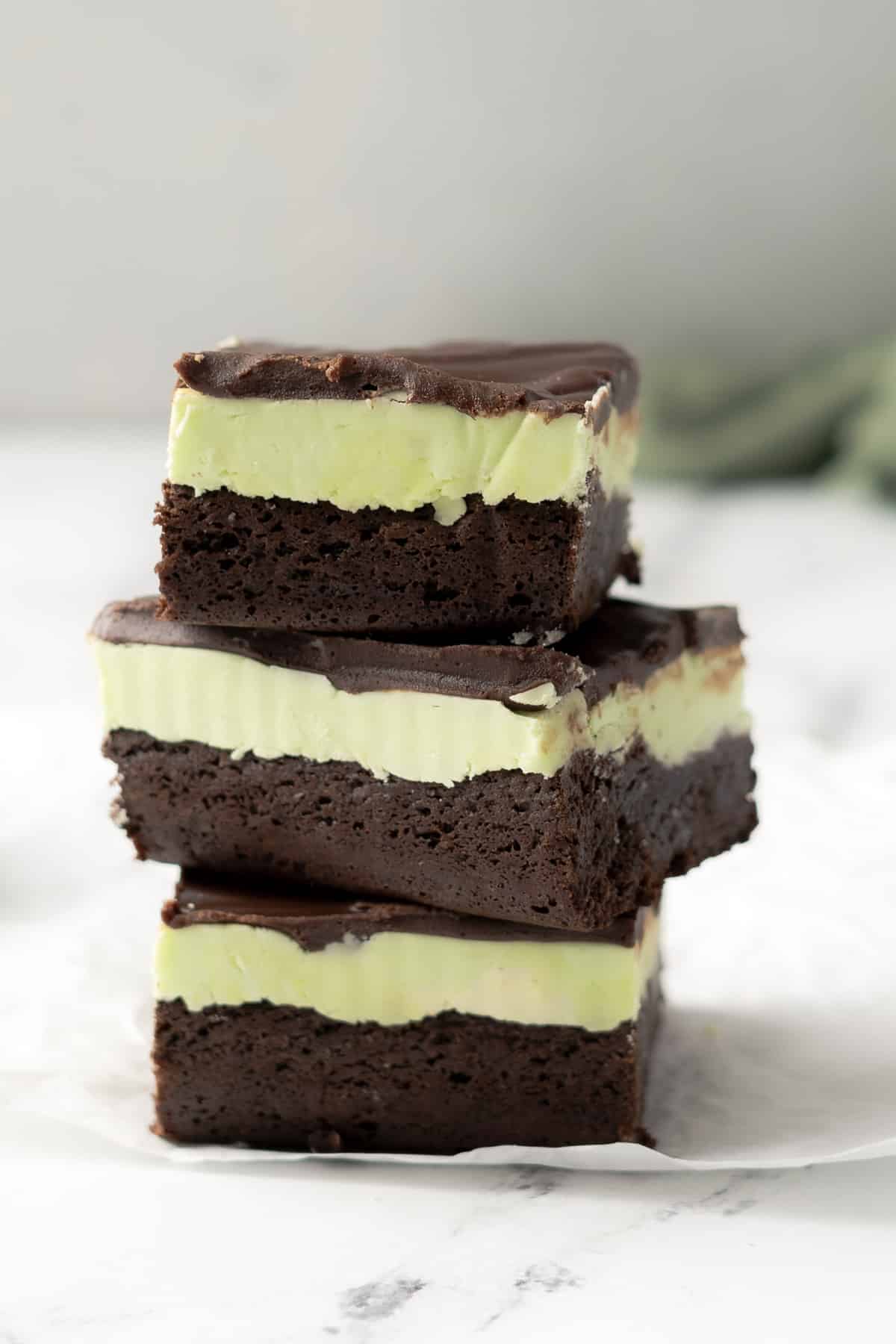 Three gluten-free chocolate mint brownies stacked on a white surface.