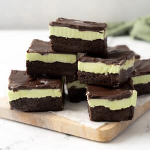 Several gluten-free mint chocolate brownies stacked on a wooden board, featuring a rich dark chocolate base, creamy green mint layer, and glossy chocolate topping.