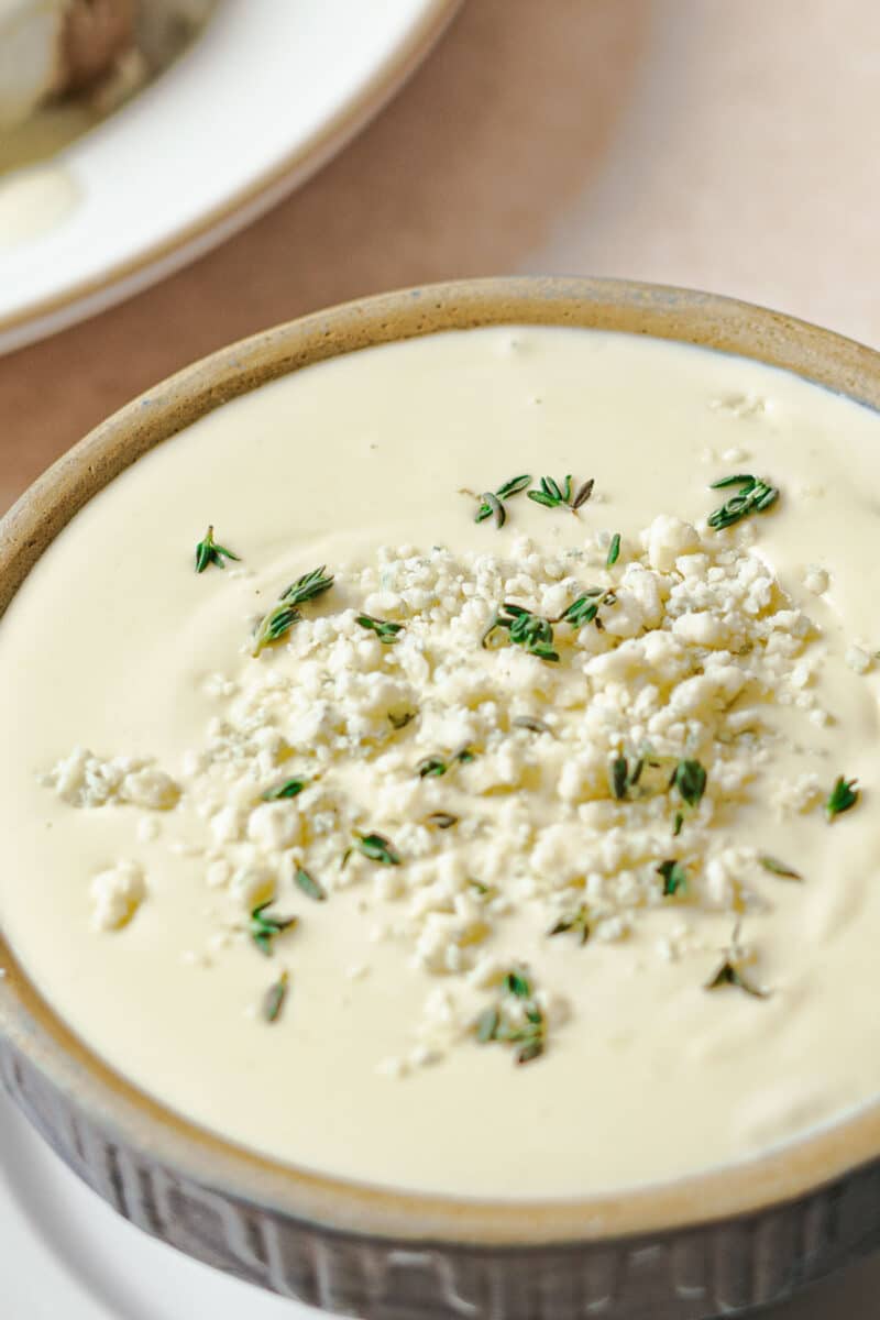 A bowl of creamy gorgonzola sauce topped with crumbled Gorgonzola and fresh herbs