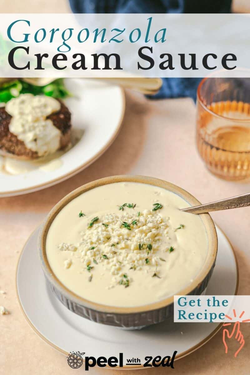 A bowl of gorgonzola cream sauce with herbs, a spoon, and a plate of steak with sauce. A glass of orange beverage is in the background. Text reads, "Gorgonzola Cream Sauce, Get the Recipe.