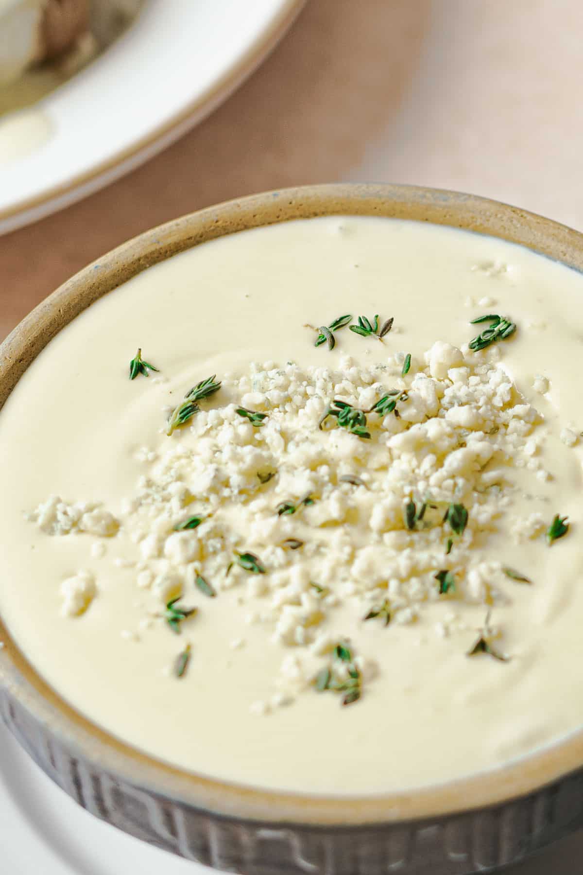 A bowl of creamy gorgonzola sauce topped with crumbled Gorgonzola and fresh herbs