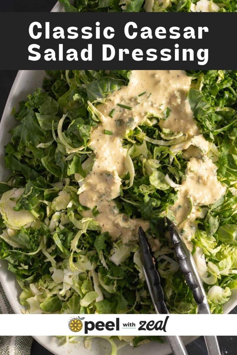 Plate of leafy greens topped with creamy Caesar dressing, with metal tongs resting on the side.