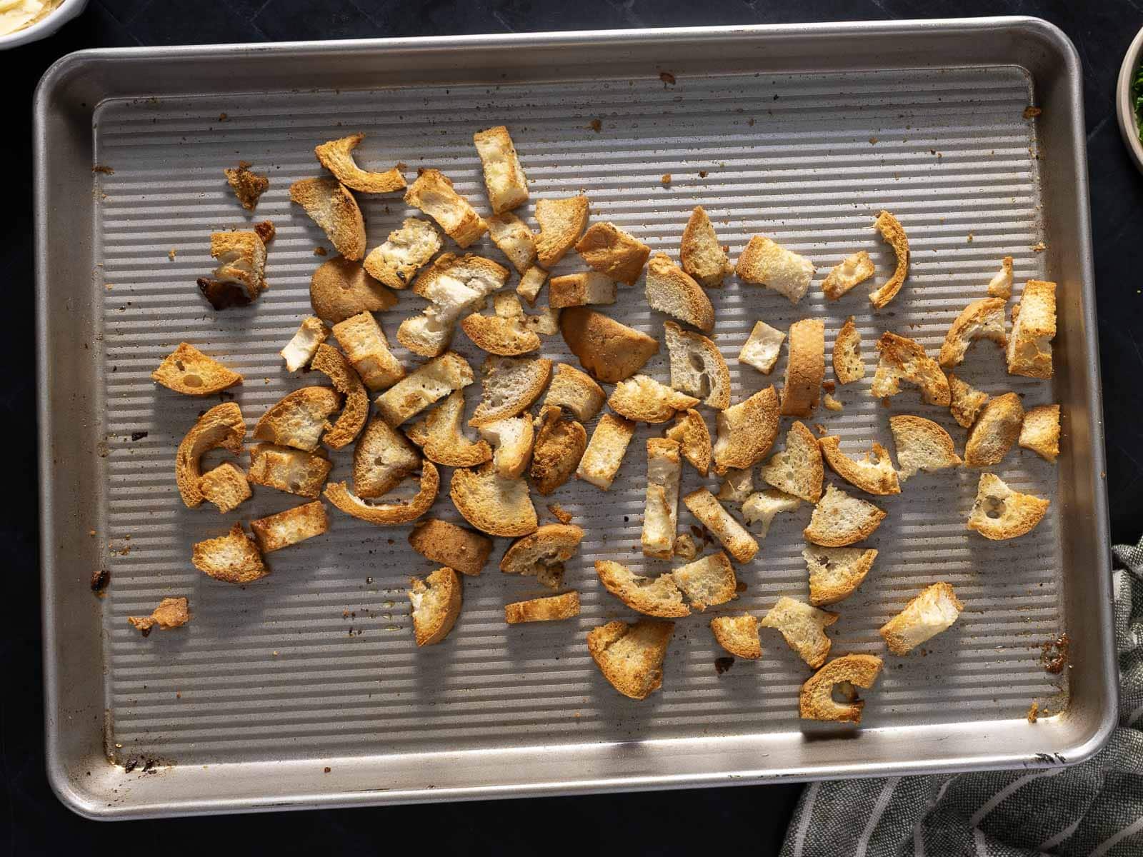 A baking sheet with small pieces of toasted bread scattered across its surface, ready to add a delightful crunch to a Caesar Salad.