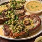 Plate of cooked lamb chops garnished with capers and green herbs, served with a creamy mustard sauce on the side—an exquisite lamb steak recipe perfect for any special occasion.