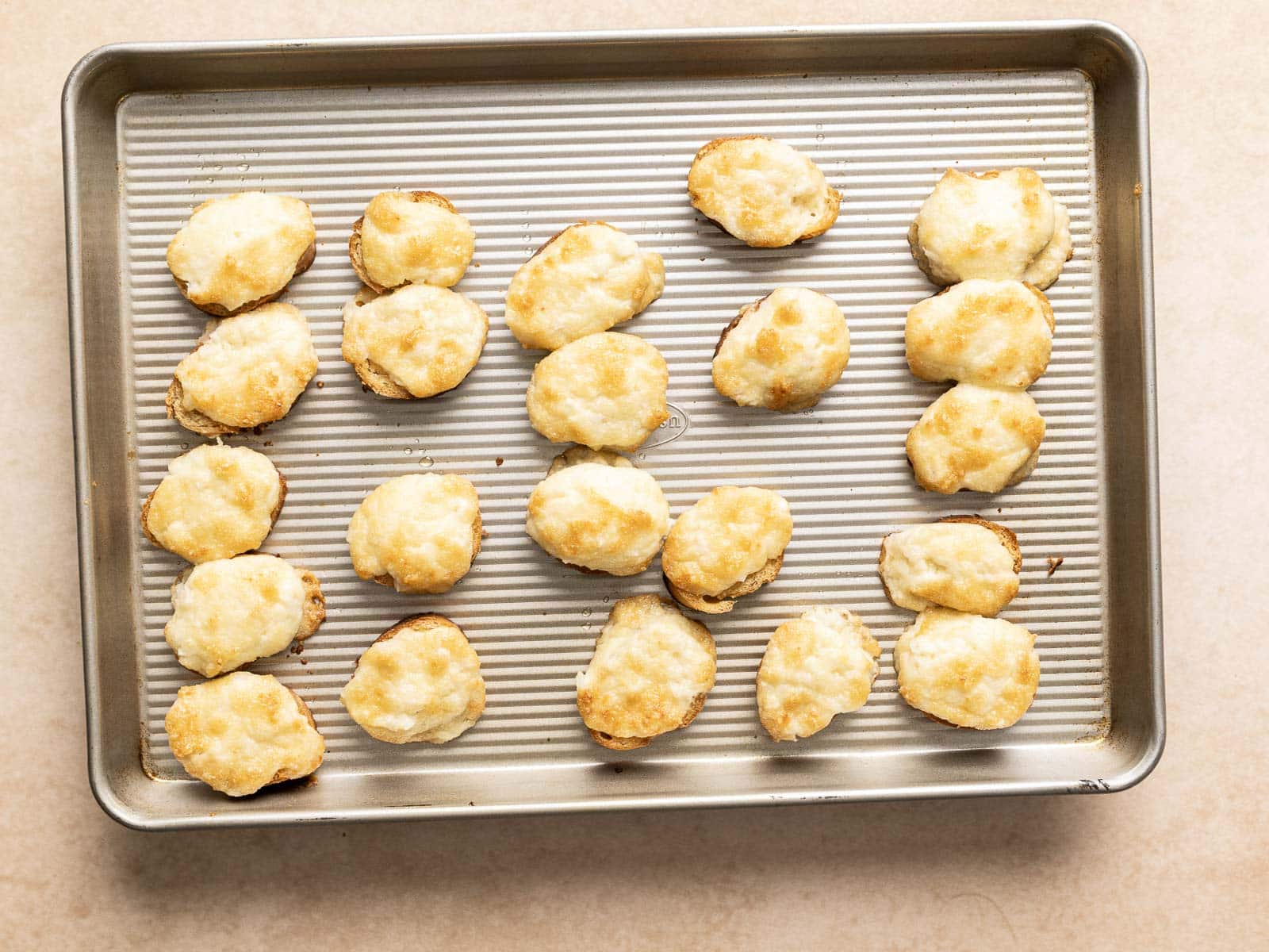 A baking sheet with twenty golden-brown cheese puffs, infused with a hint of onion, arranged in neat rows.