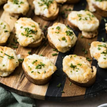 Toasted bread slices topped with melted cheese and chopped chives create a delightful recipe on a wooden serving board, perfect for any feast.
