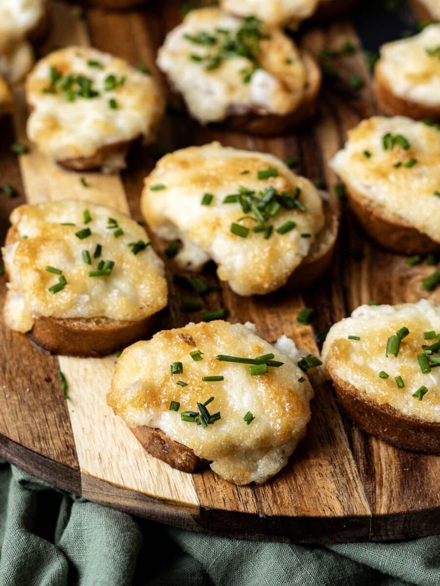 Crostini topped with melted cheese, chopped chives, and a hint of Parmesan rest invitingly on a wooden board.