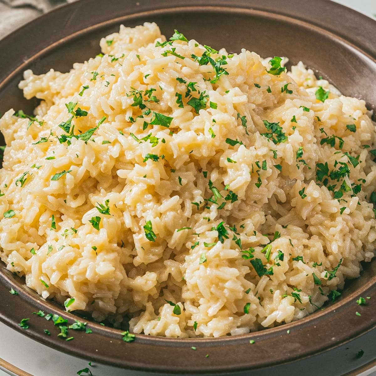 Parmesan rice in a brown bowl with fresh herbs. 