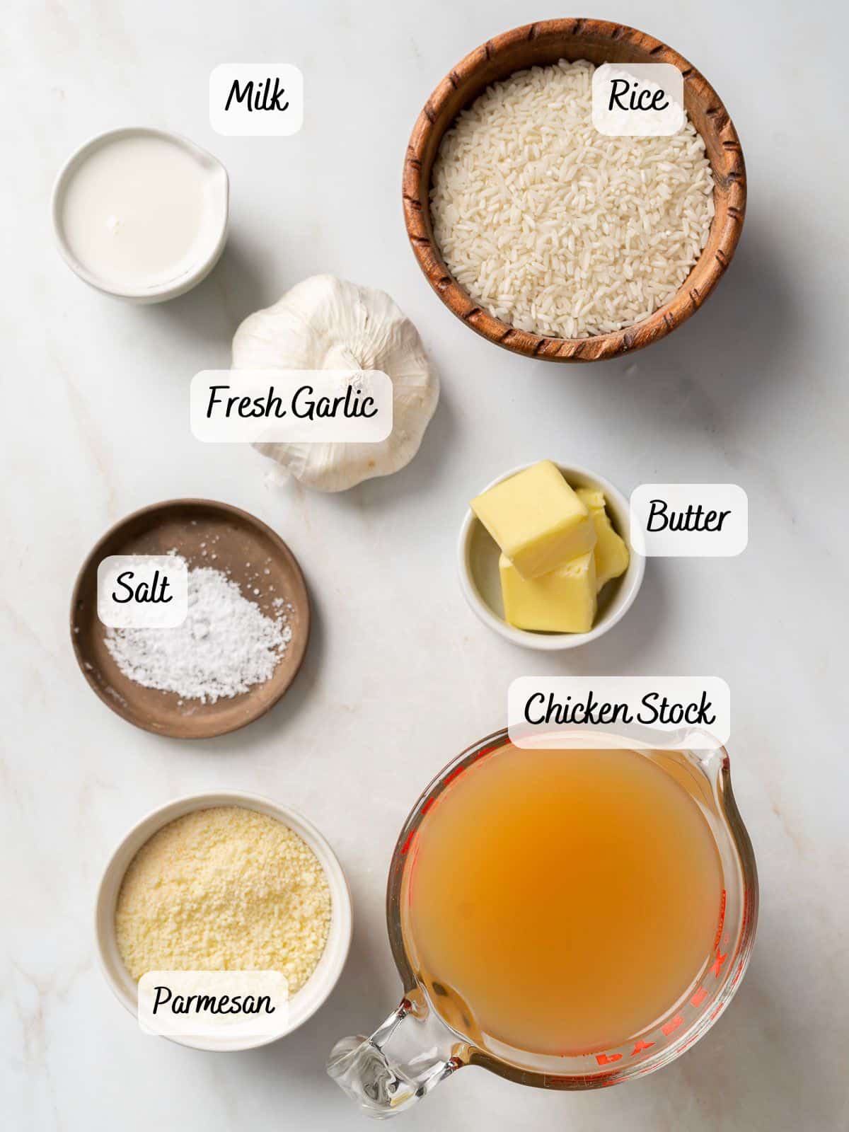 Ingredients arranged on a table include rice, fresh garlic, milk, butter, salt, chicken stock, and parmesan cheese.