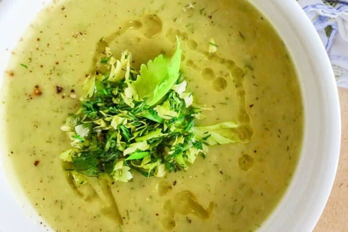 A bowl of creamy green soup garnished with fresh herbs and a drizzle of oil.
