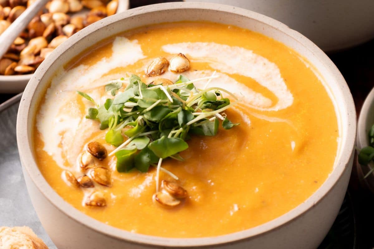 A bowl of creamy squash soup garnished with microgreens and toasted seeds.