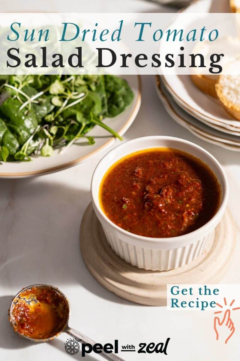 Sun dried tomato salad dressing in a white ramekin, with spinach salad and bread on the side. Text overlay promotes recipe.