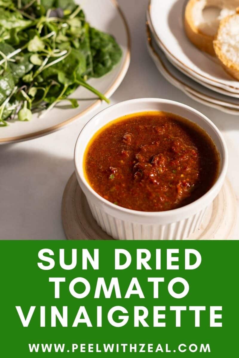 A bowl of sun-dried tomato vinaigrette on a table, accompanied by a plate of leafy greens and bread. Text at the bottom reads, "Sun Dried Tomato Vinaigrette," with a website link.